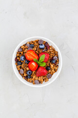 Bowl of chocolate granola with blueberries and strawberry on grey top view. Healthy breakfast. Flat lay minimalist design. Space for text. - 441646669