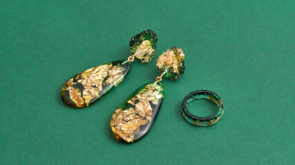 Close up shot of set of a ring and dangle earrings made of epoxy resin with golden foil inside isolated over green background