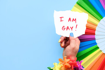 Text I am Gay on paper in hand with rainbow fan. LGBTQ community pride. Flower garland and fake...
