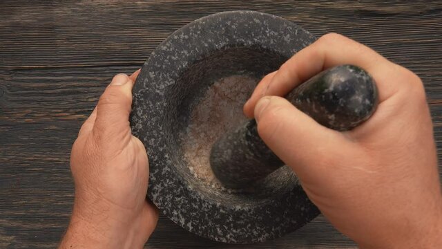 Top view of hand grinding spices and peppers in the grey stone mortar