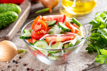 Salad of tomatoes and cucumbers in a plate and vegetables on a table. Healthy food concept