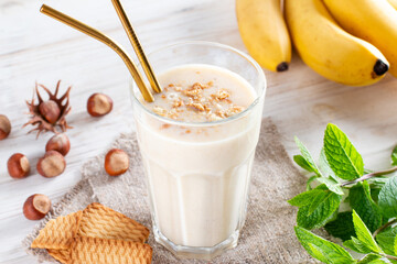 Delicious banana smoothie with sliced bananas and cookies in glass on a white background