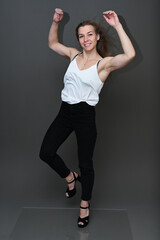 Photo in full growth of a caucasian girl in a white blouse on a gray background in the studio with a smile in a jump