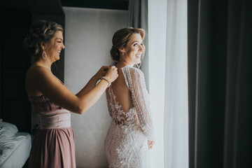 Bridesmaid helping the bride to get dressed for the wedding ceremony