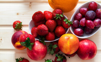Health and life benefits of strawberries, grapes, nectarines, oranges; high angle photo of fruit on traditional wooden background