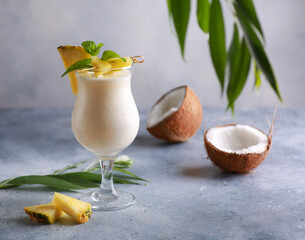 Summer. Drinks and cocktails. Pina colada in glass with pineapple, coconut, mint and a branch of greenery on a light gray background. Background image, copy space