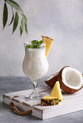 Summer. Drinks and cocktails. Pina colada in glass with pineapple, coconut, mint and a branch of greenery on a light gray background. Background image, copy space