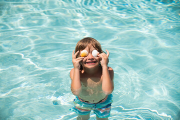 Child relaxing on the beach against blue sea water. Summer vacation and kids travel concept. Covered eyes with shells.