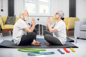 Side view of healthy and active retired couple sitting on yoga mat face to face and meditating with closed eyes. Concept of people, sport and retirement.