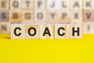 word coach is written on wooden cubes on a bright yellow surface, concept