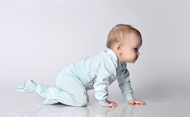 Naklejka premium Active creeping child with concentrated reproduction of the face. Small kid in blue bodybush scan on white studio background. Newborn child growth, development and study of the environment.