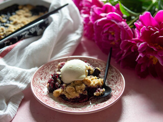 Berry crumble with ice cream on plate. Pink background with lilac peonies. Copy space. Closse up