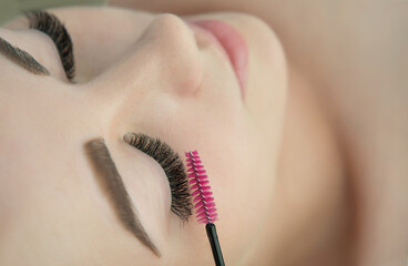 Close up of beauty model's face during procedures of eye lash extension and master’s hand with tweezers, selected focus.