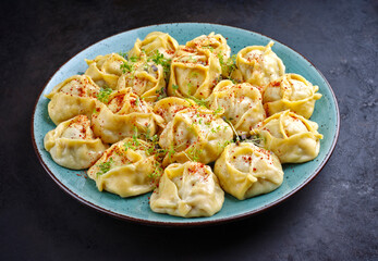Traditional steamed Kazakh manti garnished with mincemeat and sumah served as close-up on a Nordic design plate with copy space