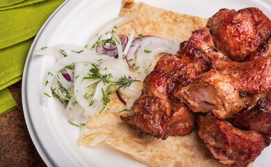 Meat cooked on skewers. Suvlaki. Shish kebab on a plate with fresh onion rings and pita bread. Grilled meat.
