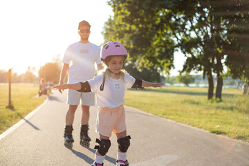 Fototapeta premium Child girl roller skating with dad in the park. Family time, activity, sport.