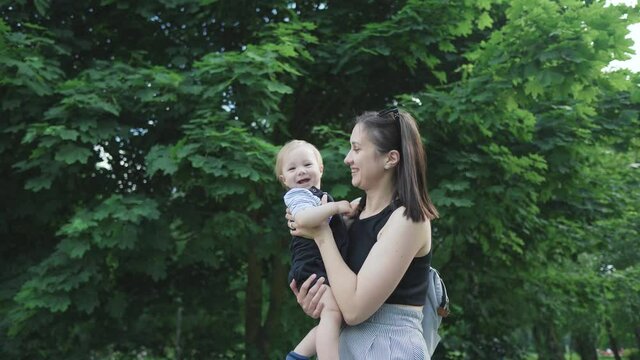 Cheerful mother having fun with her little son in Easter day, nature background. Single parent, motherhood, baby concept. Playful young mom lifting baby. Millennial Woman throwing, tossing child - Powered by Adobe