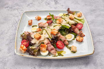 Caesar salad with herbs chicken bacon eggs and tomatoes on a square light plate, on a light background