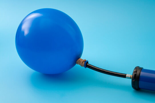 Party accessory, fun decoration and financial bubble with pump inflating a latex balloon isolated on blue background with copy space on the blank balloon