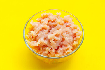 Minced meat of chicken fillet in glass bowl on yellow background.