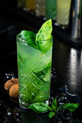 Refreshing summer cocktail with green basil, kiwi fruit and ice on black background