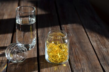 Glass jar with vitamins in yellow gelatin capsules and a glass of water.