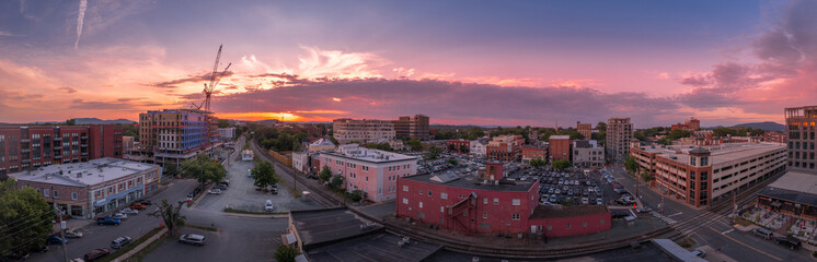 Fototapeta na wymiar Aerial sunset view of downtown Charlottesville, Virginia with new construction office apartment building, city market parking lot, parking garage and the mall with dramatic colorful purple orange sky 