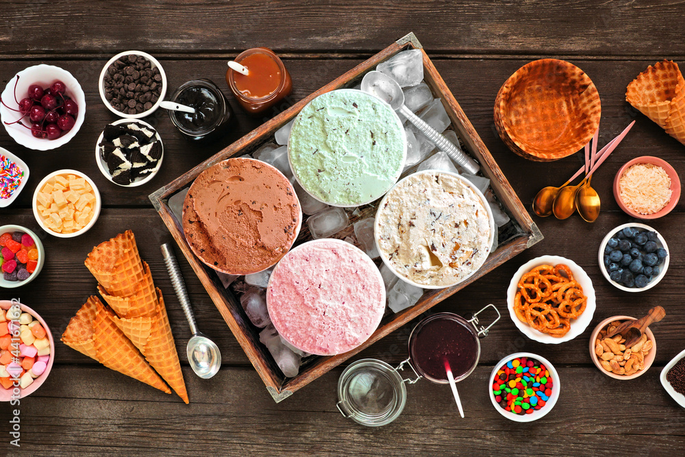 Poster summer ice cream buffet with a mixture of flavors and sweet toppings. top view table scene on a dark
