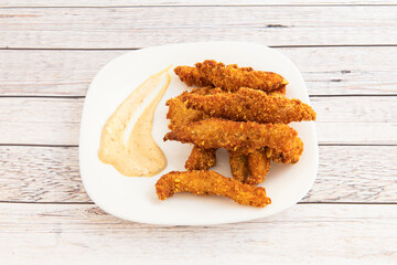 Plate of chicken fingers in batter with egg and breadcrumbs accompanied by sauce for dipping