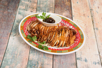 Whole roast duck with crispy skin, served in fillets with sauce to accompany it cooked in a Chinese restaurant and placed on a wooden background