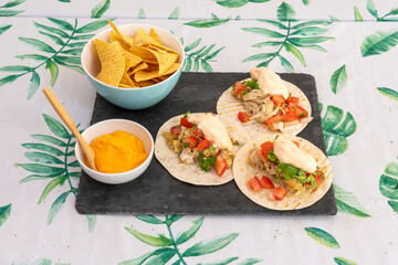 Mexican menu with three chicken tinga tacos and corn nachos in a bowl for dipping with melted cheddar cheese