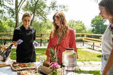 Caucasian woman standing by the female sommelier in sunny summer day talking about food and wine...