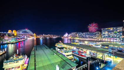 Panoramic night view of Sydney Harbour and City Skyline of circular quay the bridge  nsw Australia.  bright neon lights reflecting off the water And fireworks in the night skies 