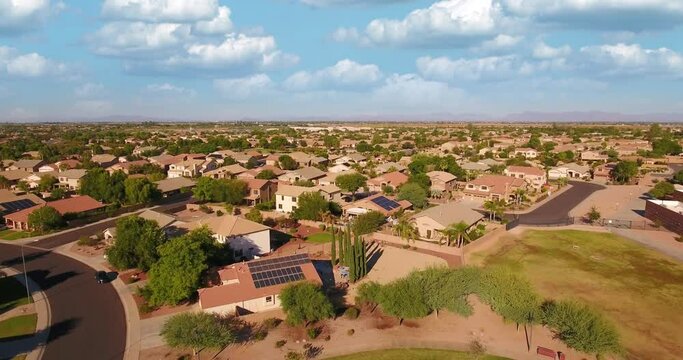 A flyover aerial establishing shot of a typical Arizona residential neighborhood. The Superstition Mountain range in the distance. Tilt up to summer cloudscape sky. Phoenix suburb.	