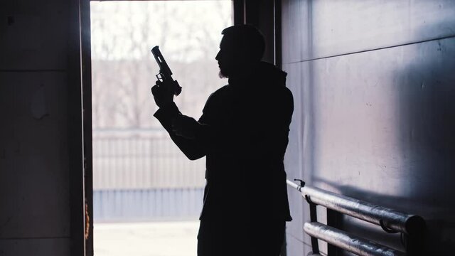 The dark silhouette of the man pulls the shutter of the gun and goes forward
