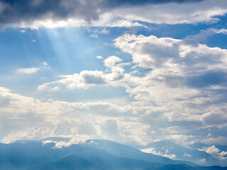 6月下旬、雲間から差し込む光芒と山並みの風景
