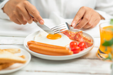 Obraz na płótnie Canvas women holds a fork and knife eating breakfast.fried egg,sausage,bacon,toast bread,orange juice.
