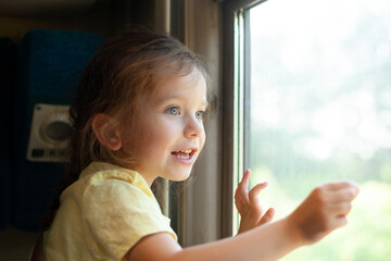 A little girl looks out the train window with interest. Travelling with a child. vacation....
