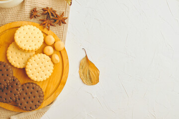 Cookies and candy on wooden tray. White table with kitchen tablecloth, sweets and star anise. Autumn leaf on table. The concept of Christmas, Thanksgiving and Halloween.
