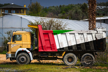 Obraz premium Dump truck with the image of the national flag of United Arab Emirates is parked against the background of the countryside. The concept of export-import, transportation, national delivery of goods