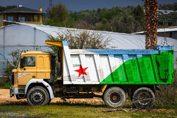 Dump truck with the image of the national flag of Djibouti is parked against the background of the countryside. The concept of export-import, transportation, national delivery of goods