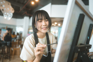 Happy young adult asian woman painting brush on canvas at workshop art lesson class.