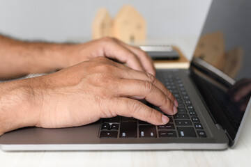 A man sits at a desk and is using a laptop computer. concept working from home, online, use of technology, online shopping, freelancing, internet. Selective focus, closeup, white blurred background.