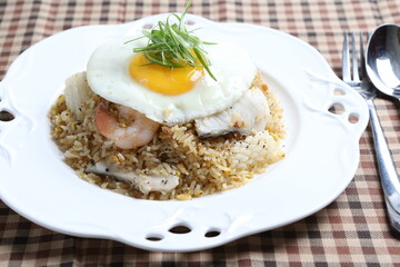 wok garlic fried rice with mixed seafood fish, prawn, squid, octopus, fried egg and vegetables on white plate asian halal menu