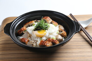 chef cook Hong Kong congee porridge with mixed seafood unagi, fish, prawn, squid, mushroom, egg and vegetables in black hot clay pot , chopstick spoon asian healthy halal menu