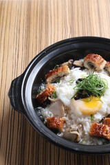 chef cook Hong Kong congee porridge with mixed seafood unagi, fish, prawn, squid, mushroom, egg and vegetables in black hot clay pot , chopstick spoon asian healthy halal menu