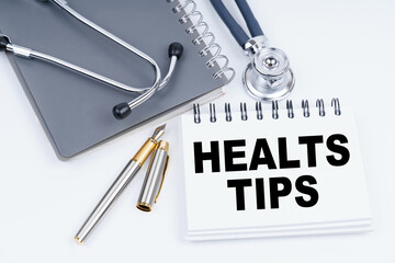 On the table are a stethoscope, a pen and a notebook with the inscription - HEALTS TIPS