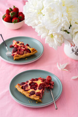 Table with a pink tablecloth, a bouquet of peonies and a sweet strawberry pie, pieces of pie on plates, a delicious summer dessert