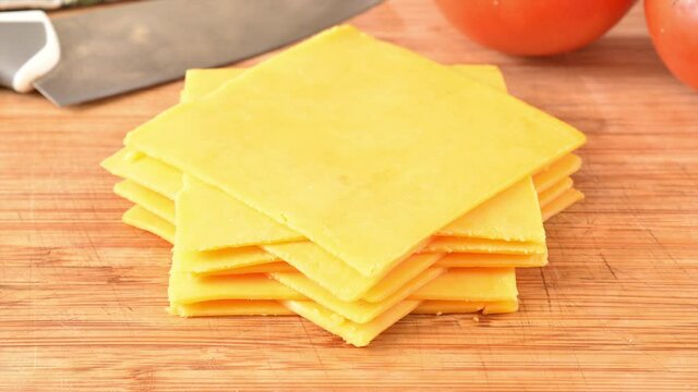 Cheddar cheese slices stacking on a cutting board, stop motion animation
