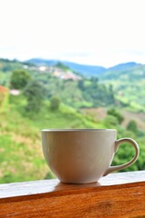 Coffee mug on wooden terrace, with mountain and sky as background.